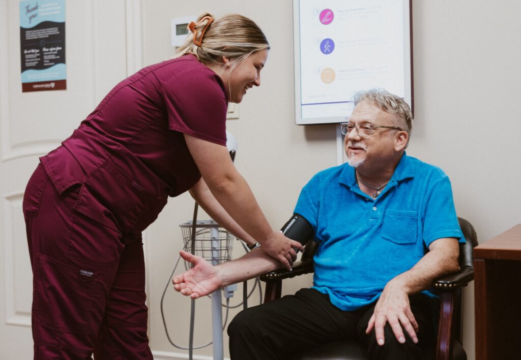Nurse in red scrubs taking blood pressure of male patient in a bright blue shirt