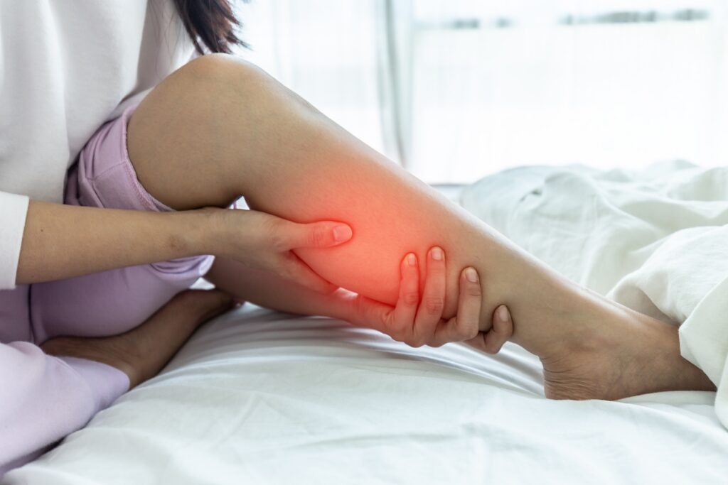 Woman sitting in bed, holding calf to illustrate leg pain